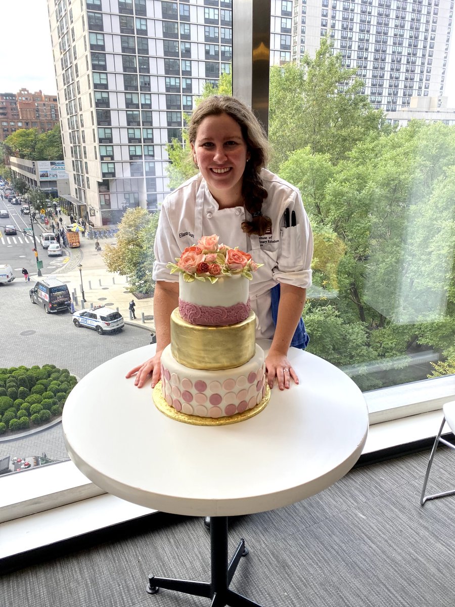 Elli, the baker behind Elli's Desserts, in chef whites beside a three-tier fondant cake